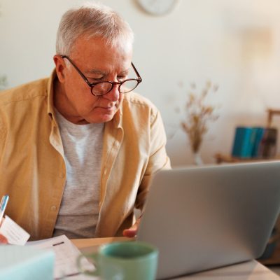 Senior man using laptop checking documents indoor